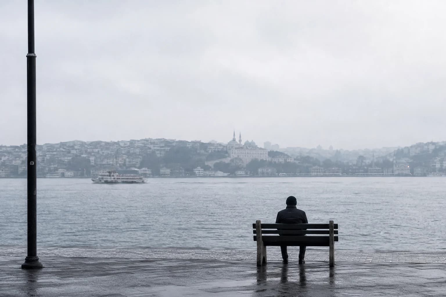 Yağmurlu bir sabah İstanbul kıyısında Boğaz'a bakan boş bir bankta oturan kişi