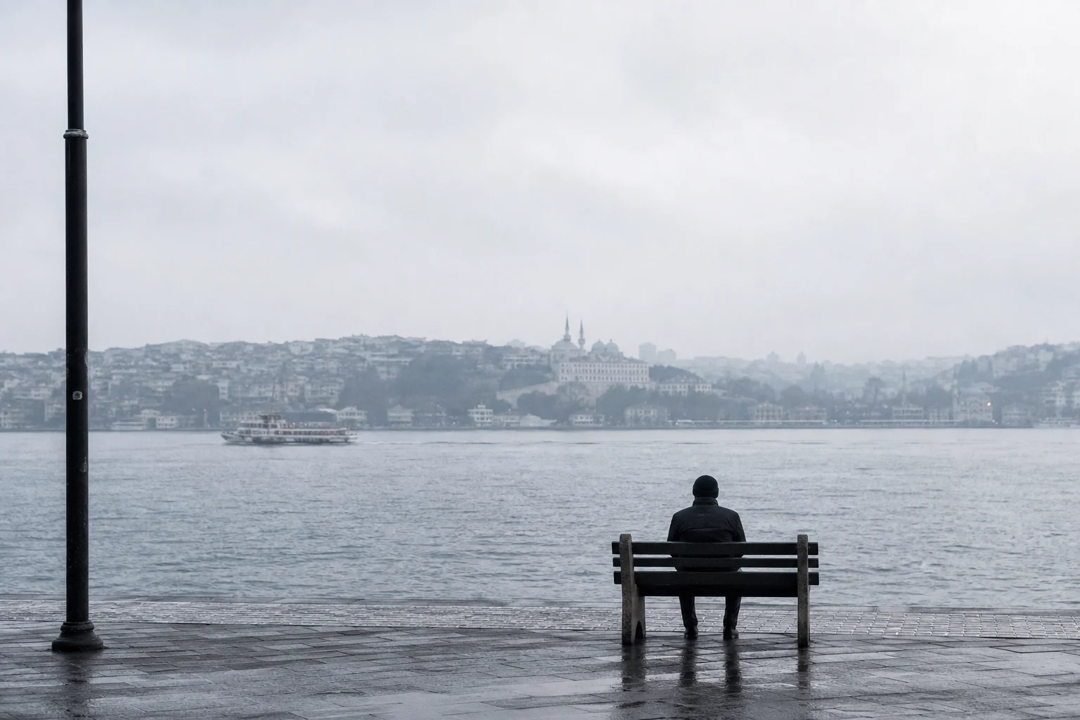 Yağmurlu bir sabah İstanbul kıyısında Boğaz'a bakan boş bir bankta oturan kişi
